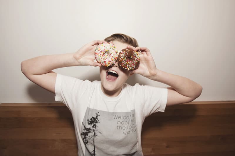 A smiling child holding two sprinkle donuts over their eyes at Coco Donuts in Portland