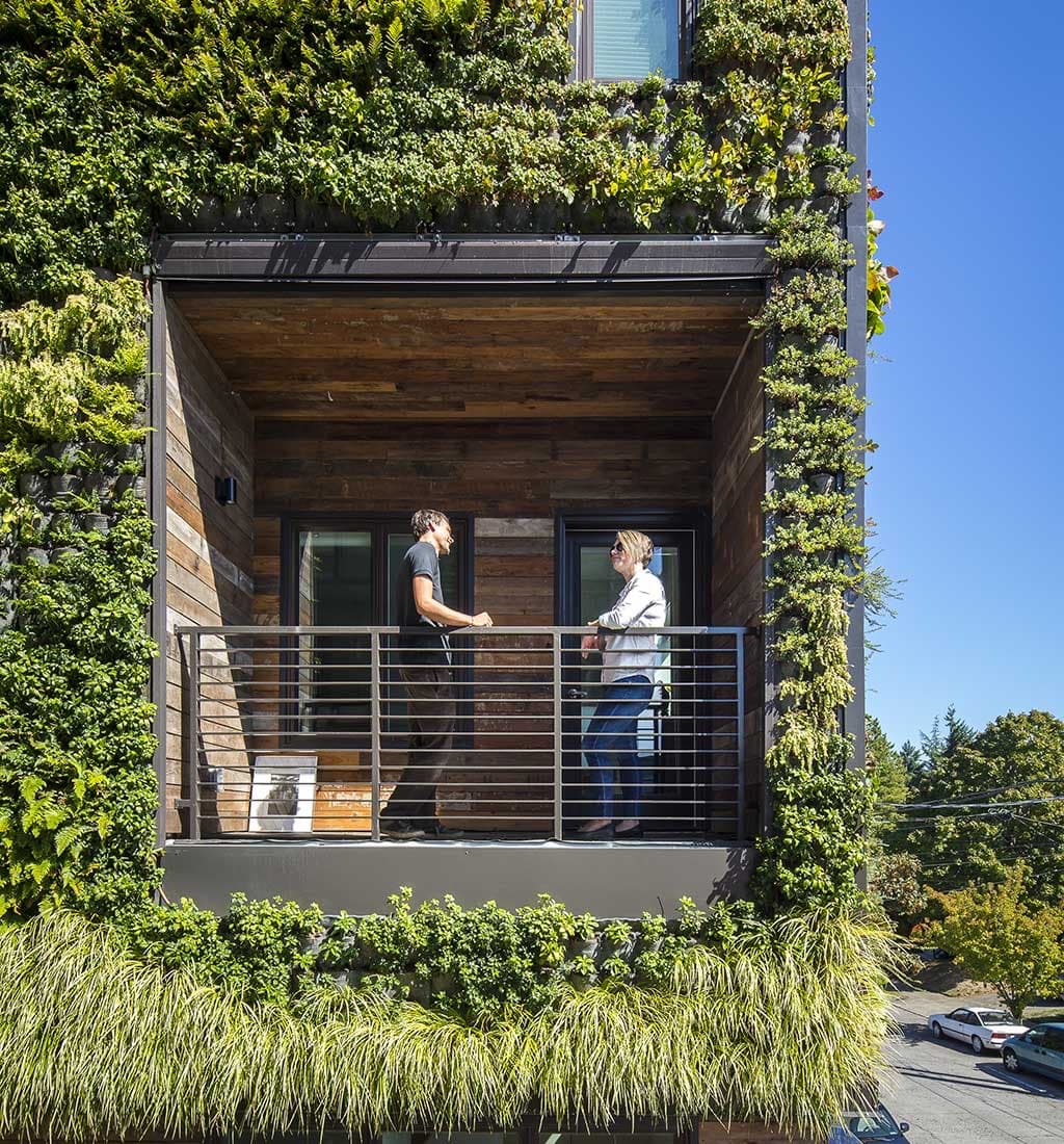 Two people talking on a balcony framed by a living wall at a SolTerra building