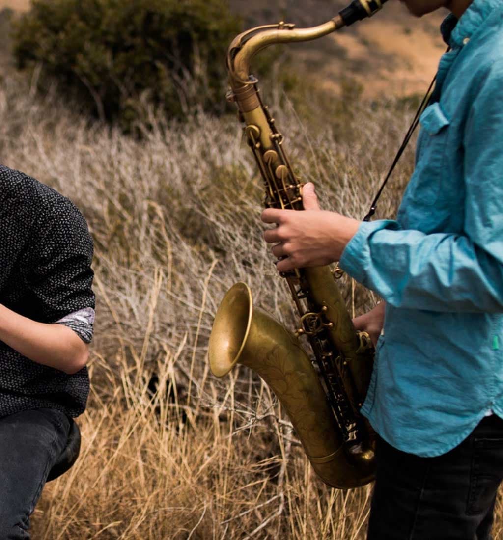 Musicians improvising outdoors, a saxophone player in a field of tall dry grass