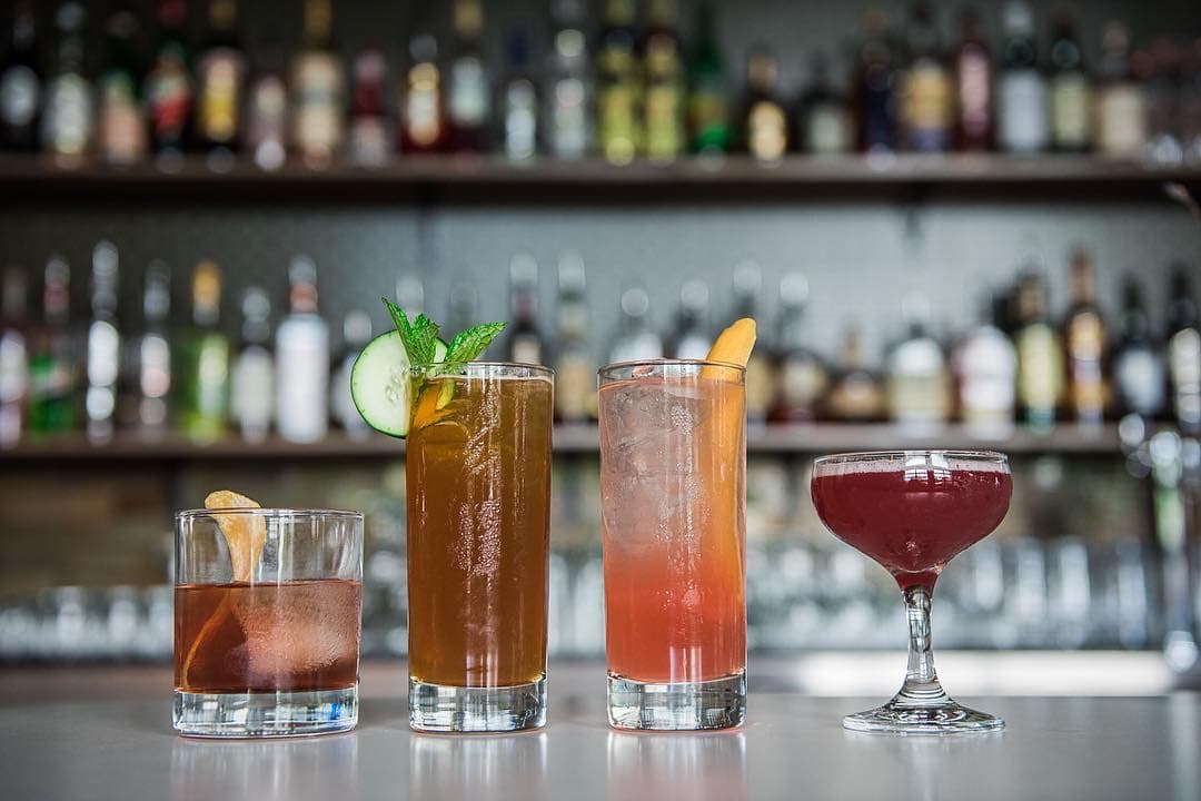 Four craft cocktails lined up on the bar in front of shelves of bottles at Grand Army Tavern