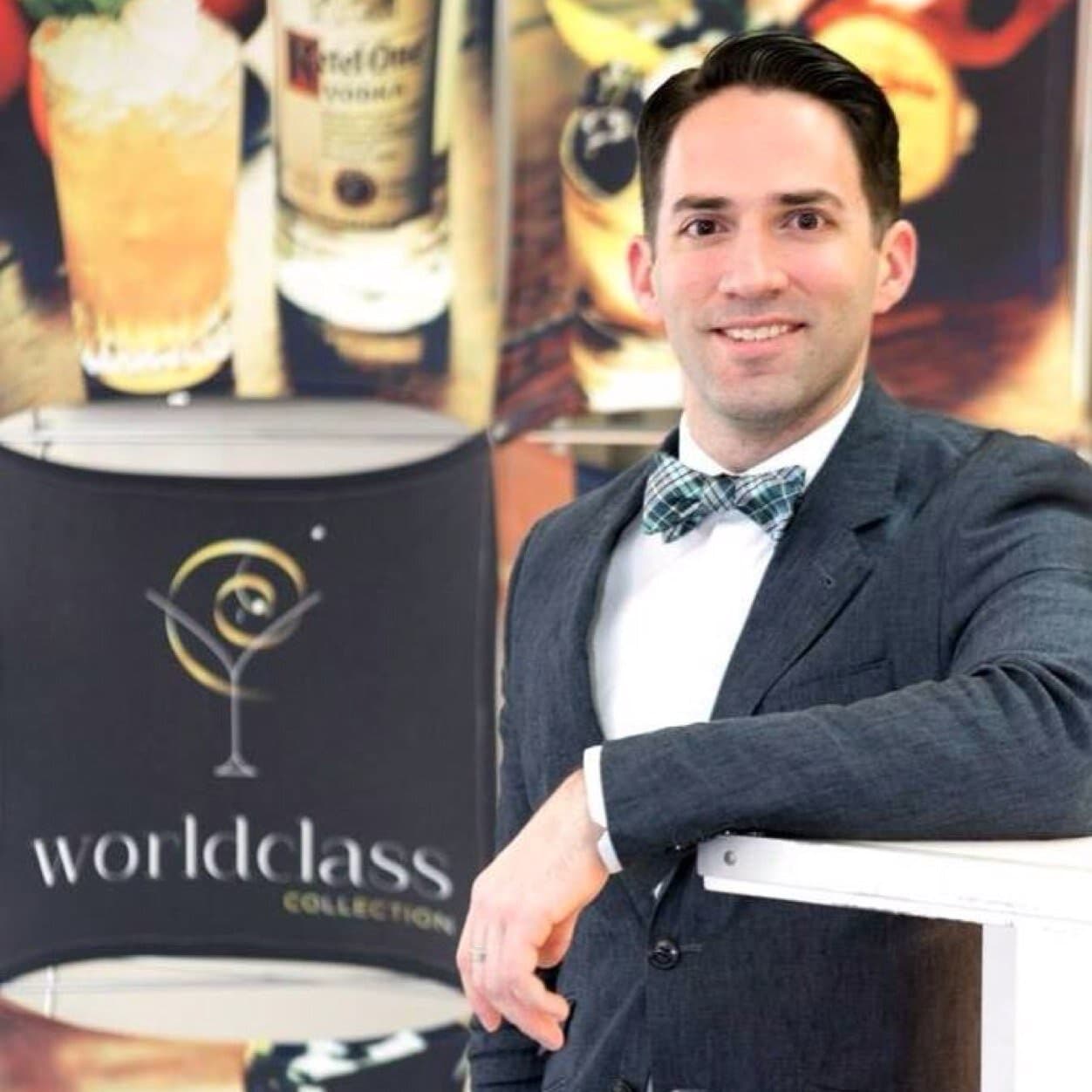 A smiling man in a suit and bow tie at a cocktail event backdrop, pictured for Palomar bar and restaurant